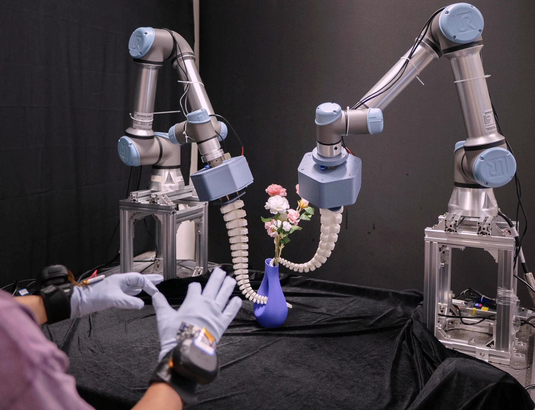 Two robot arms with compliant manipulators handling flowers beside a vase